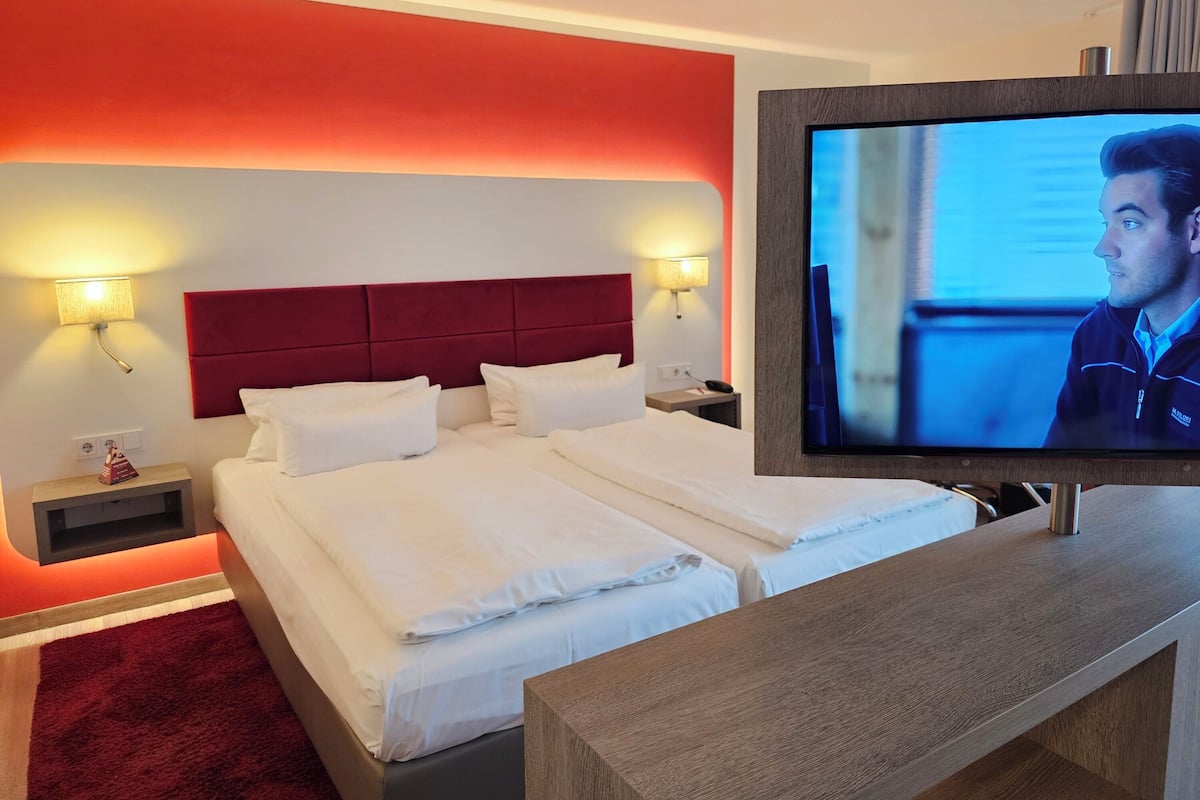 Ein Hotelzimmer mit einem großen Bett, zwei Nachttischen, einem Fernseher und einer roten Akzentwand.