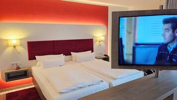A hotel room with a large bed, two bedside tables, a TV, and a red accent wall.