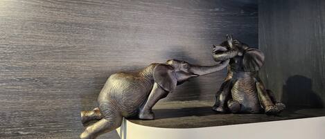 A sculpture of two elephants on a white shelf against a dark wooden wall.
