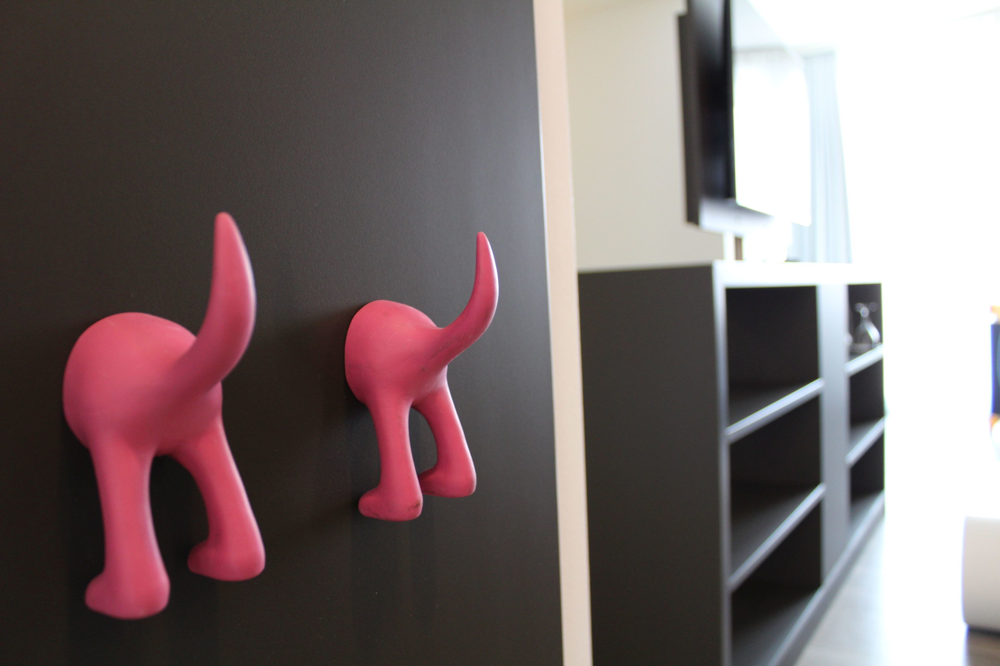 Two pink elephant-shaped wall decorations in a modern room with a black wall and a TV mounted above a black shelving unit.