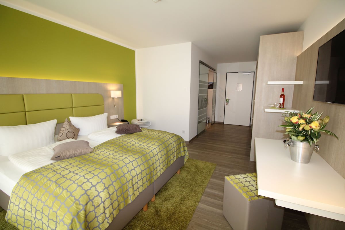 Ein Hotelzimmer mit einem Bett, einem Nachttisch und einer kleinen Schreibtischzeile mit einer Pflanze.