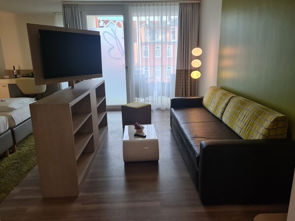 Una sala de estar moderna con un televisor de pantalla plana, un sofá, una mesa de centro y una mesita con un control remoto.