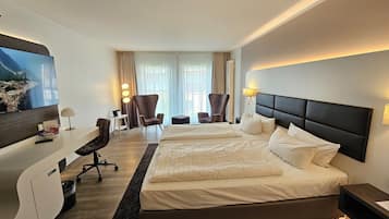 Habitación de hotel con una cama grande, escritorio, silla, televisión y ventana con cortinas.