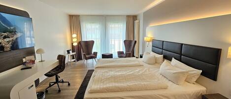 Habitación de hotel con una cama grande, escritorio, silla, televisión y ventana con cortinas.