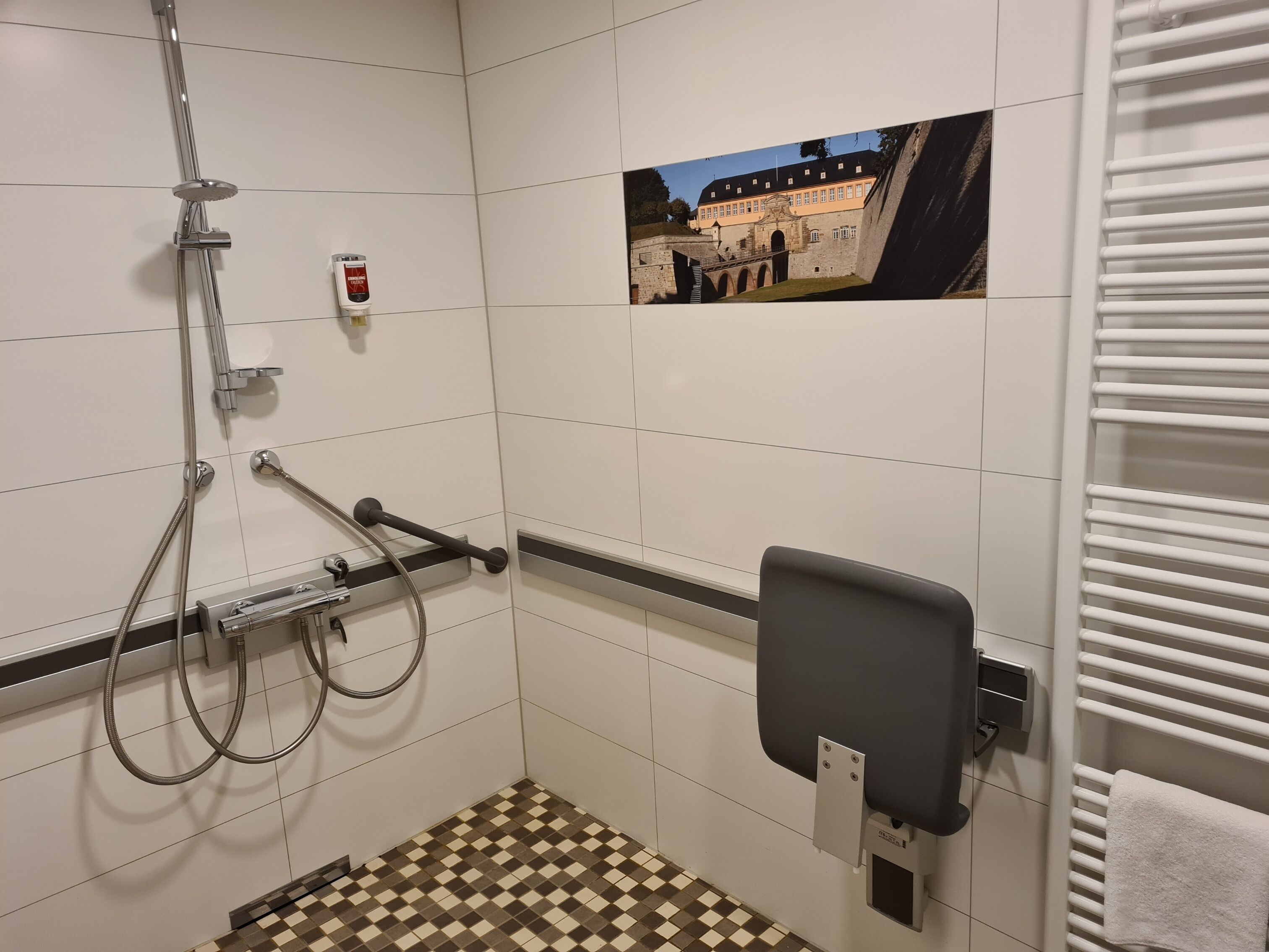 A bathroom with a shower, a hand dryer, a towel rack, and a check-in counter.