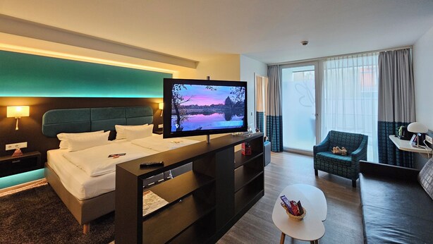 Una habitación de hotel moderna con cama, televisor, sofá y una pequeña mesa.