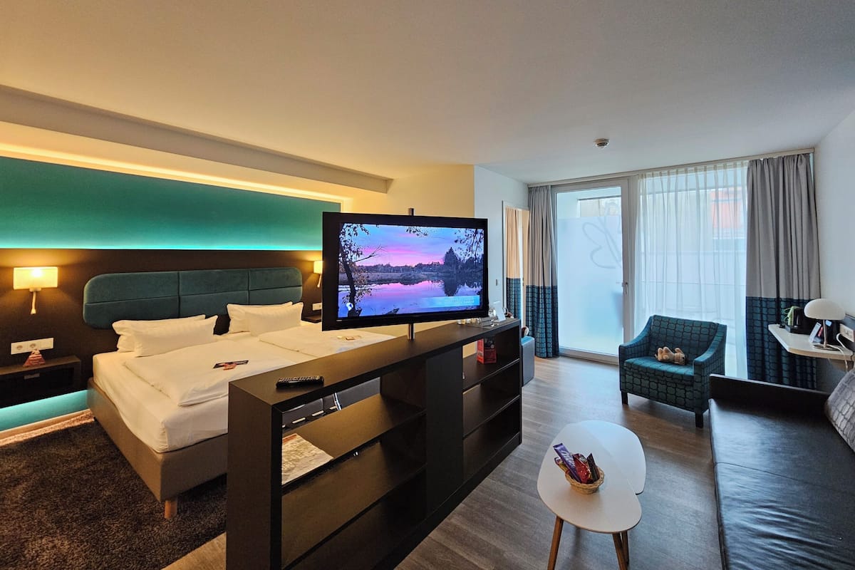 Ein modernes Hotelzimmer mit Bett, Fernseher, Sofa und einem kleinen Tisch.