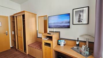 A hotel room with a wooden wardrobe, a desk with a computer, a TV, and a framed picture on the wall.