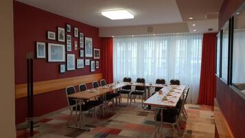 A conference room with a long table, chairs, framed pictures on the wall, and a large window with curtains.