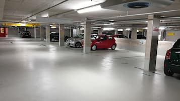 Eine mehrgeschossige Tiefgarage mit geparkten Autos in markierten Stellplätzen, deutlicher Beschilderung und tragenden Säulen.