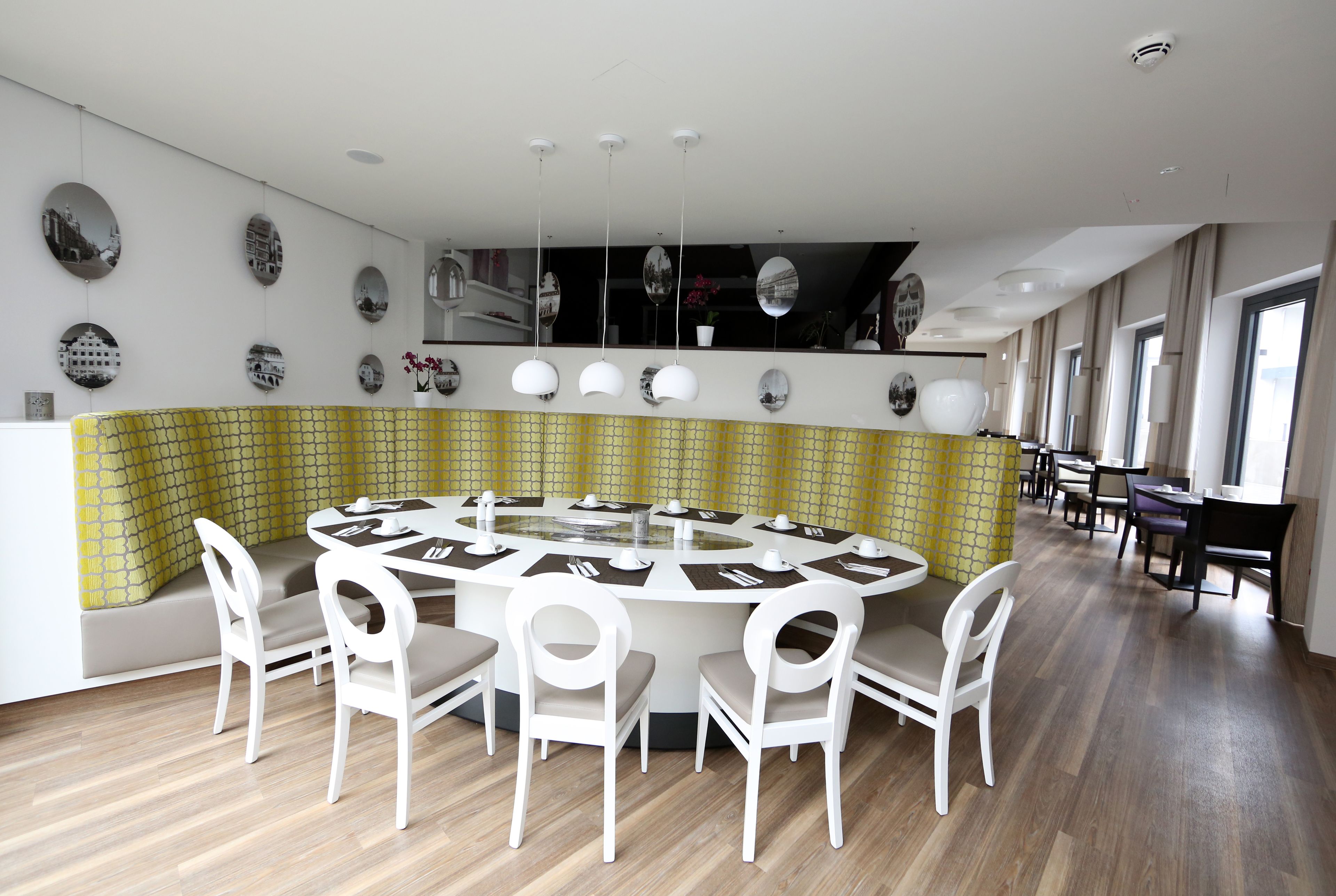 A modern dining area with a round table, white chairs, and a yellow patterned wall.