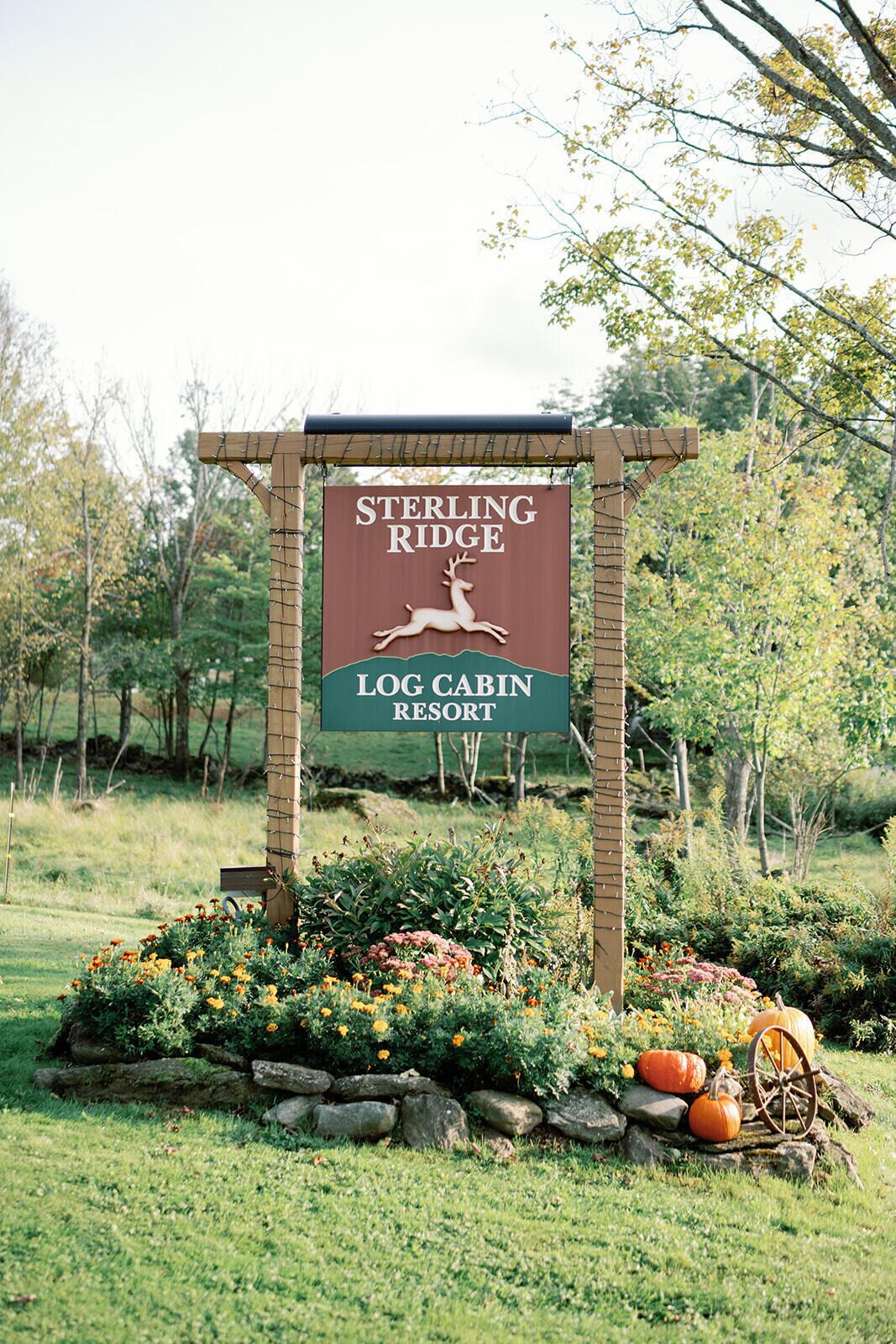 Letrero del Resort Cabañas de Madera Sterling Ridge con un logotipo de ciervo, rodeado por un jardín con flores y calabazas.