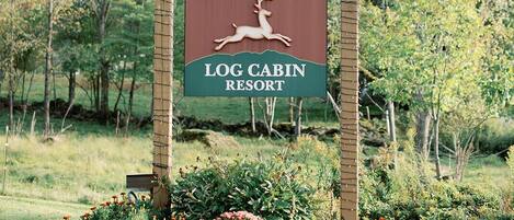 Letrero del Resort Cabañas de Madera Sterling Ridge con un logotipo de ciervo, rodeado por un jardín con flores y calabazas.