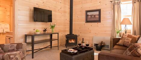 A cozy cabin interior with a fireplace, seating area, and a flat-screen TV mounted on the wall.