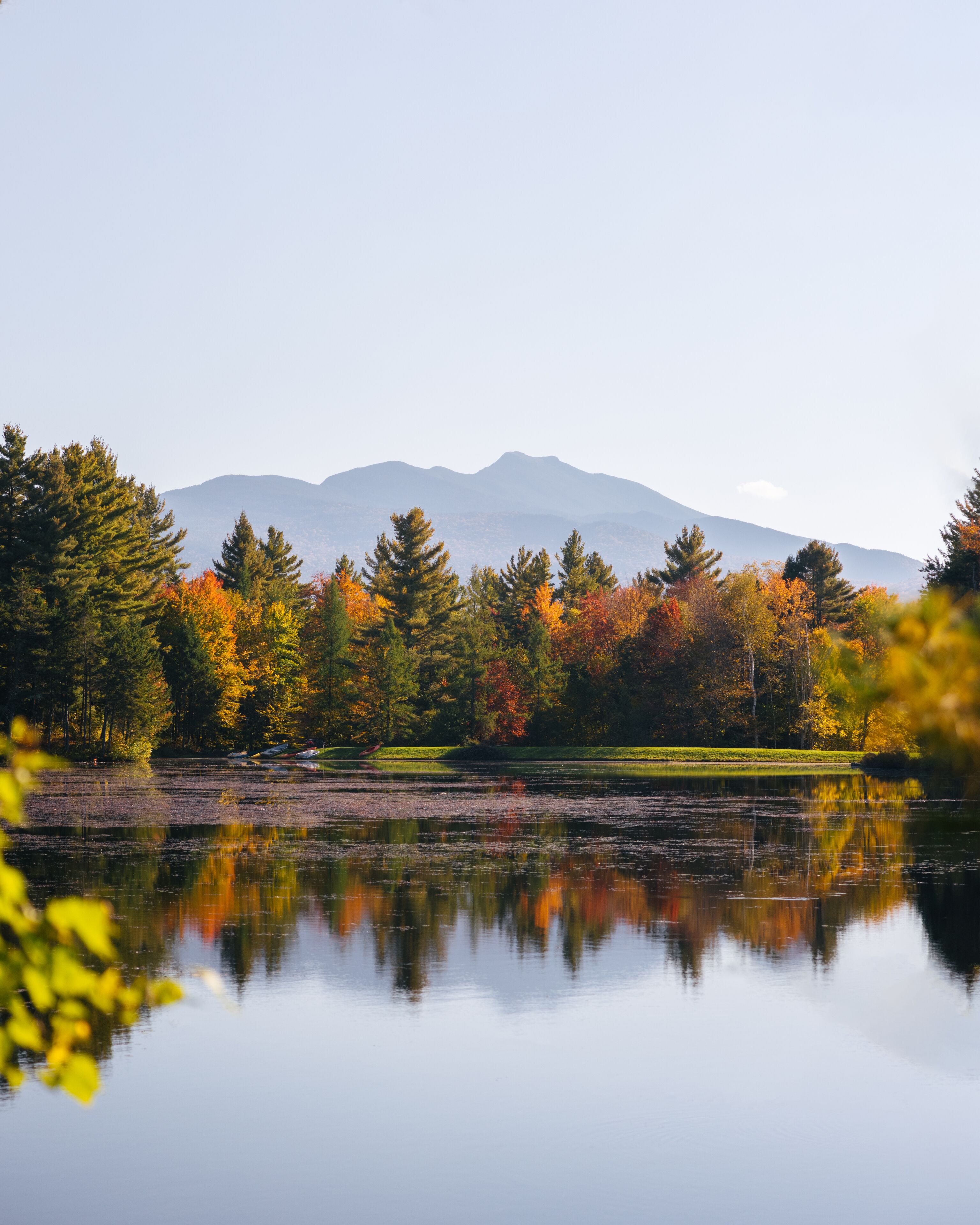 Un lac paisible où se reflètent les arbres aux couleurs automnales, avec une montagne en arrière-plan.