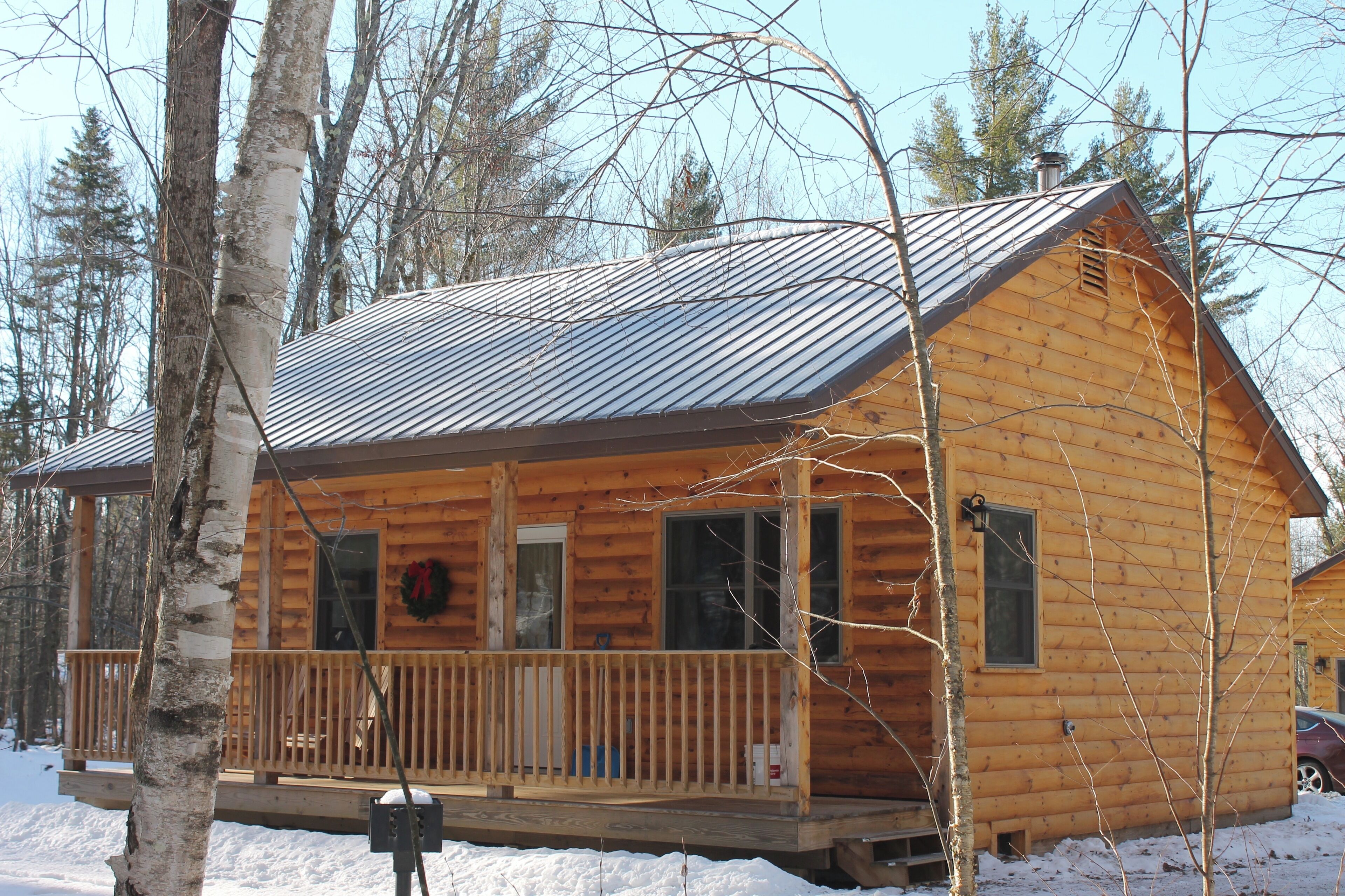 A wooden cabin with a metal roof, a wooden deck, and a front porch.