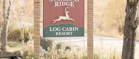 A sign for Sterling Ridge Log Cabin Resort with a deer logo, surrounded by autumn foliage and pumpkins.