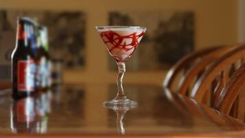 A martini glass with a red and white pattern on a reflective surface, a bottle of beer, and wooden chairs in the background.