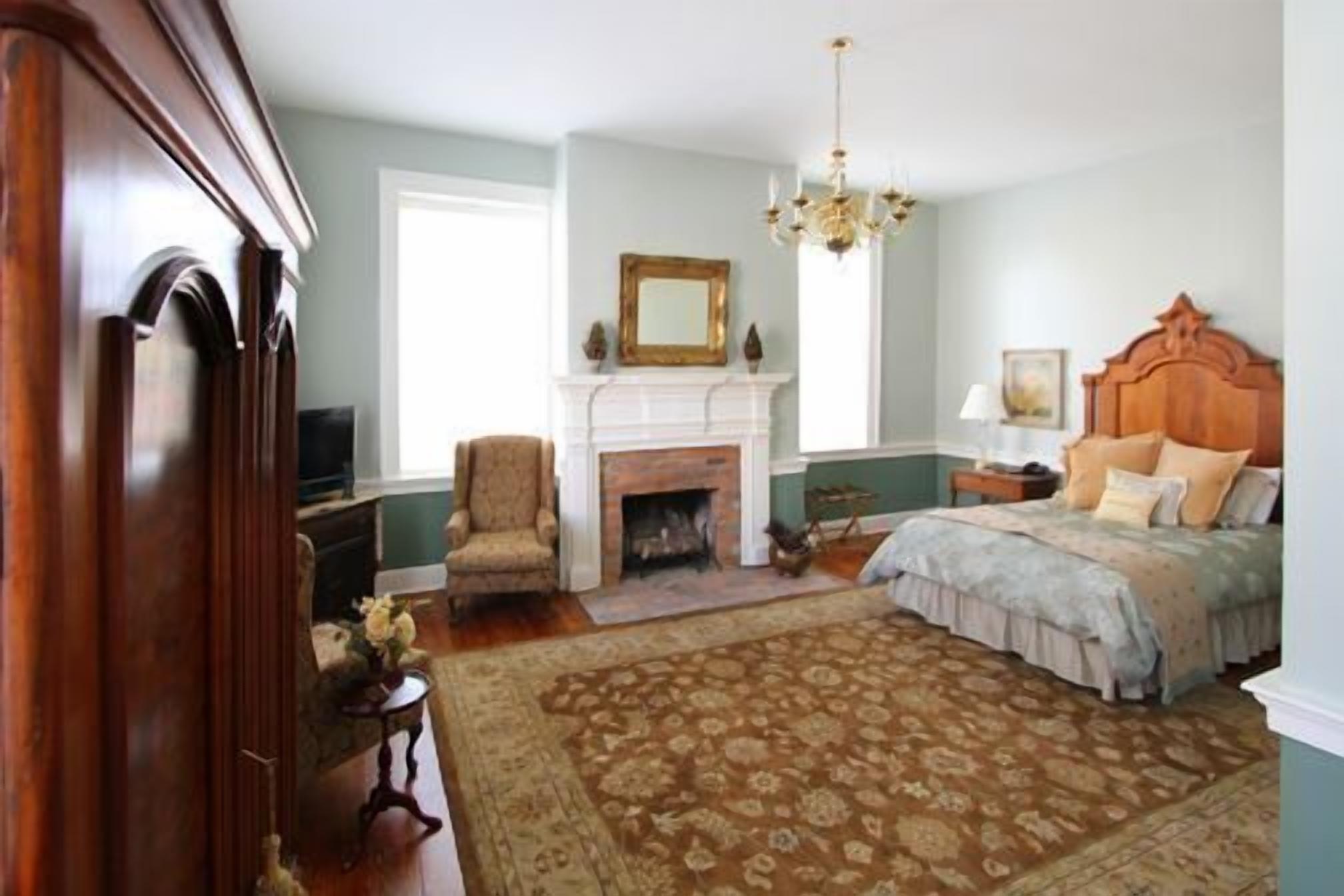 A bedroom with a fireplace, a bed with a wooden headboard, a chair, and a chandelier.