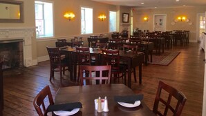 A spacious dining area with multiple tables and chairs, a fireplace, and wall-mounted lighting fixtures.