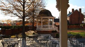 An outdoor patio area with metal tables and chairs, a gazebo, and a brick building in the background.