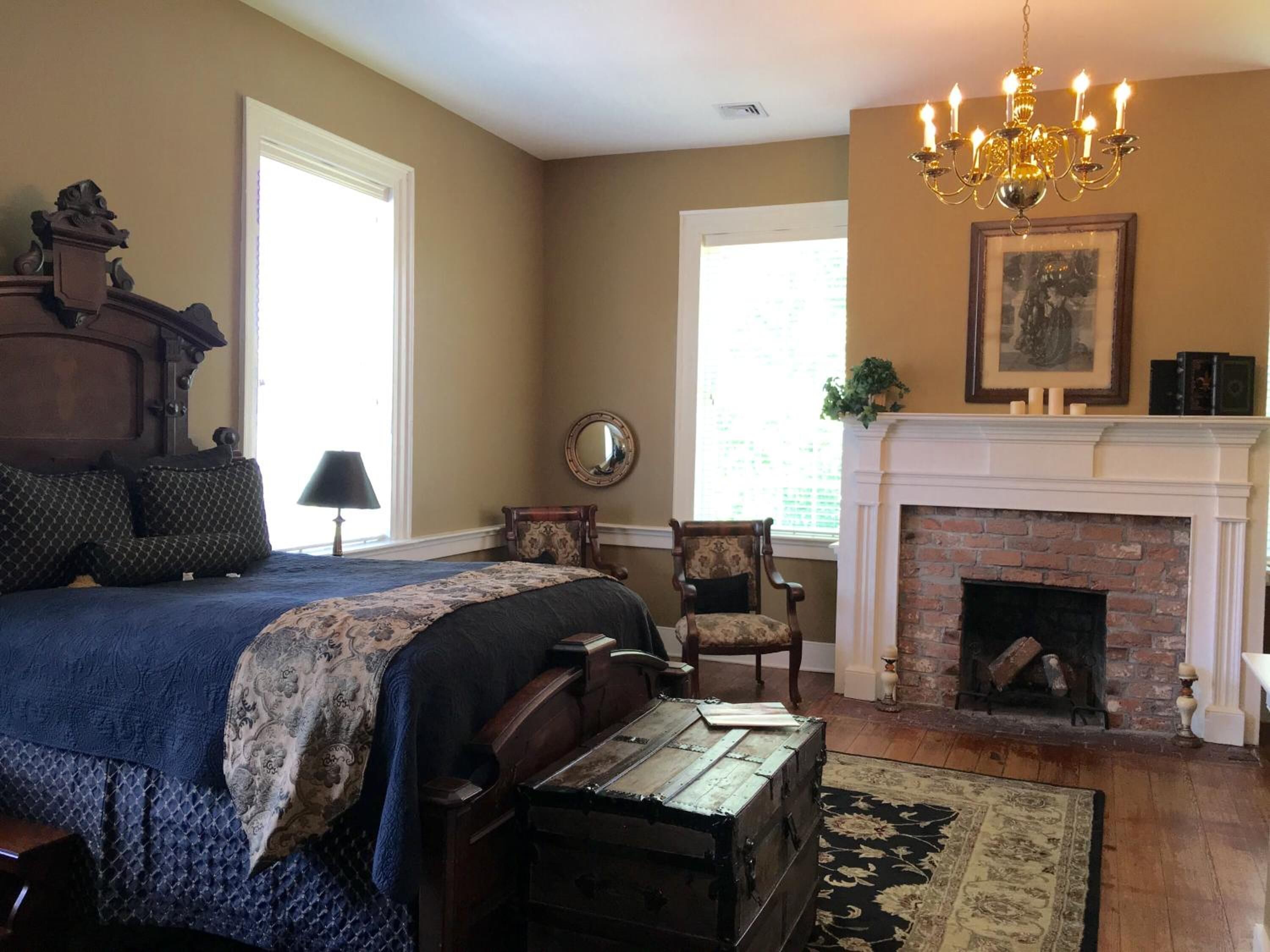 Une chambre à coucher avec un grand lit, une commode en bois, une chaise, une cheminée et un lustre.