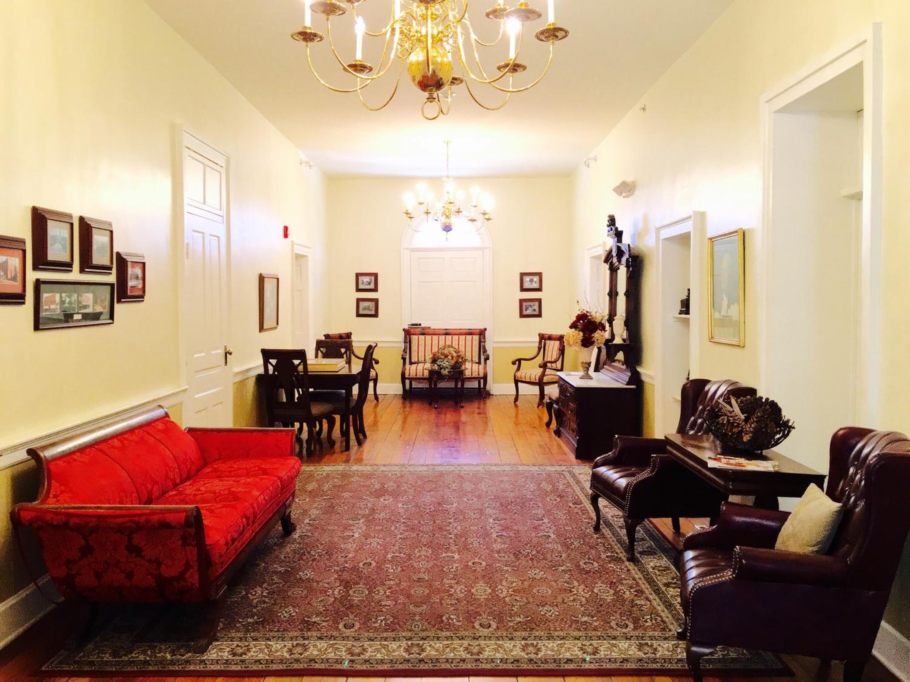 A spacious living room with a red sofa, a patterned rug, and a chandelier.