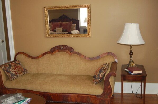 A room with a wooden sofa, a matching armchair, a small table with a lamp, and a mirror on the wall.