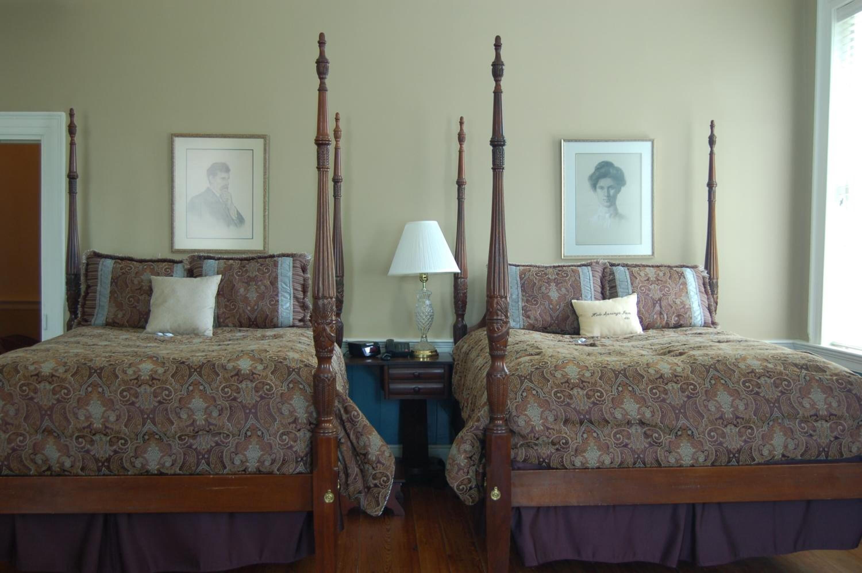 Un dormitorio con camas con dosel, una mesita de noche con lámpara y retratos enmarcados en la pared.