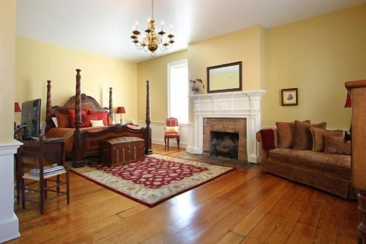 A spacious living room with a large wooden floor, a four-poster bed, a fireplace, and a comfortable sofa.