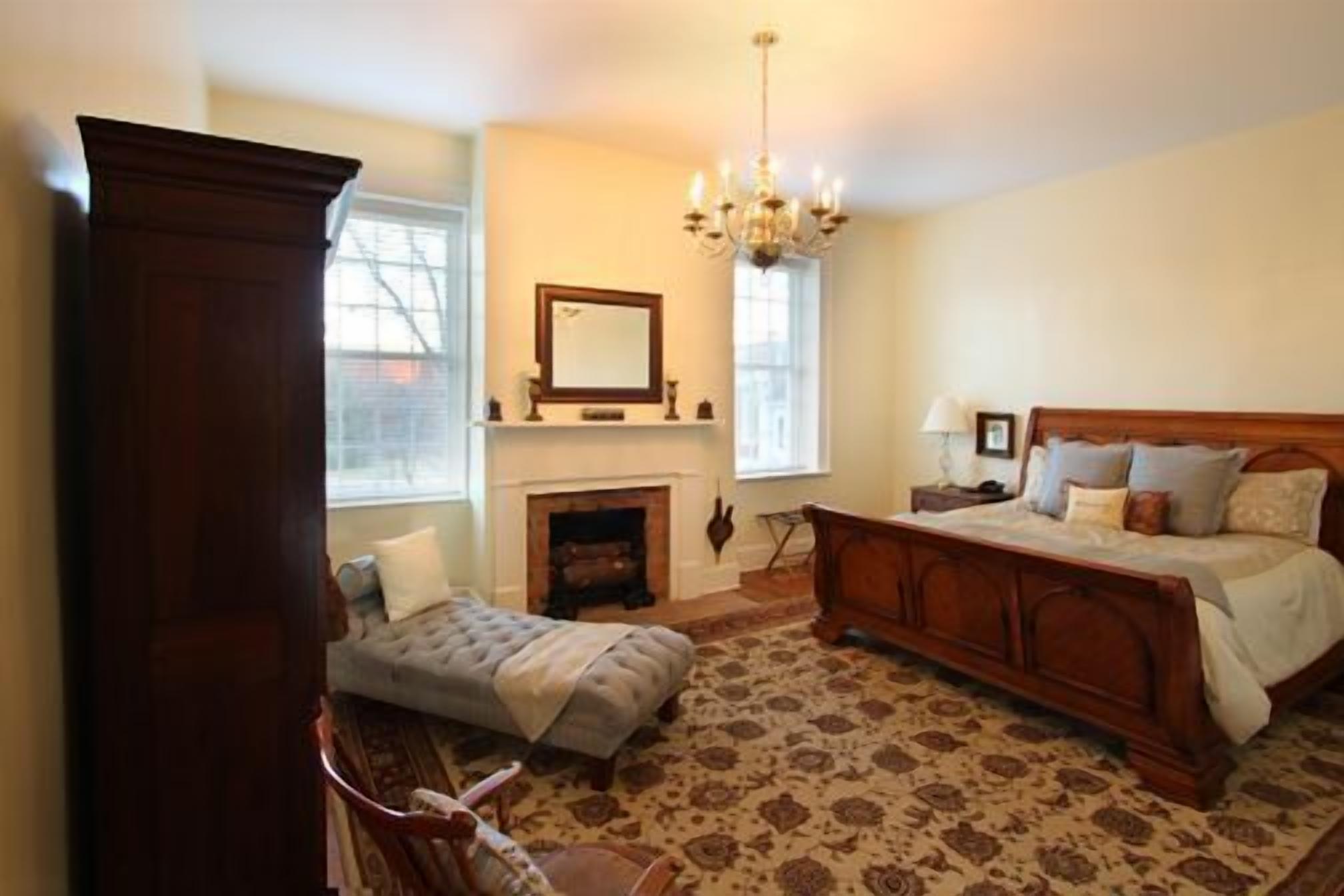 Un dormitorio con una cama grande, un sofá más pequeño, una chimenea y un candelabro.
