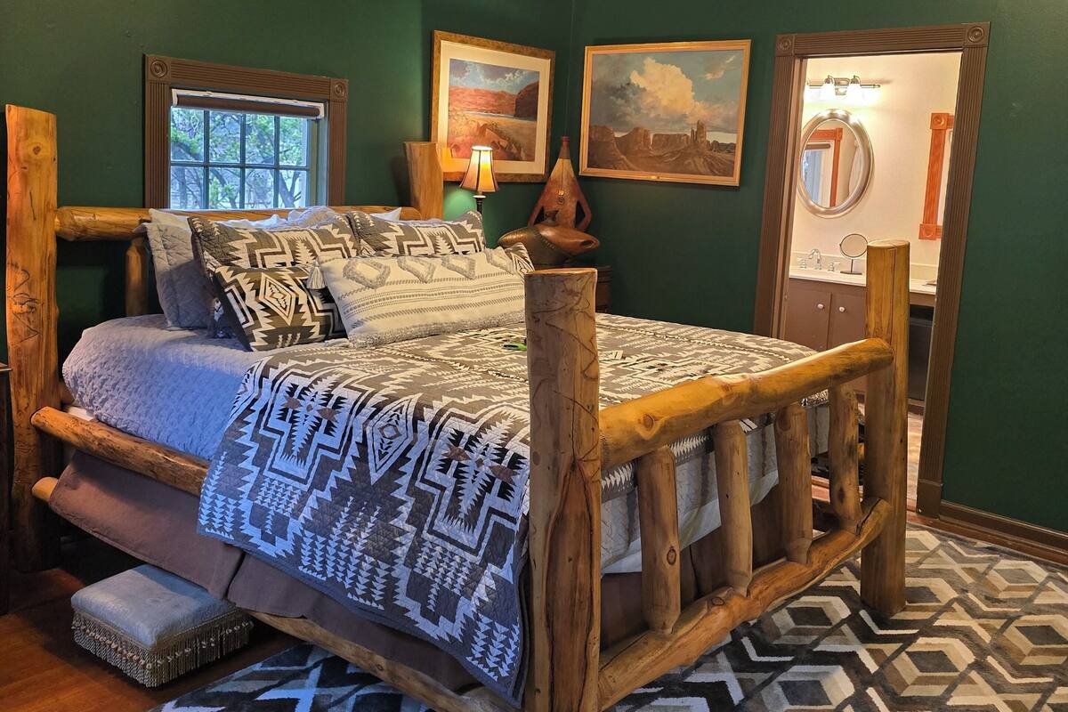 Een kamer met een houten bed, een raam, een schilderij en een spiegel.
