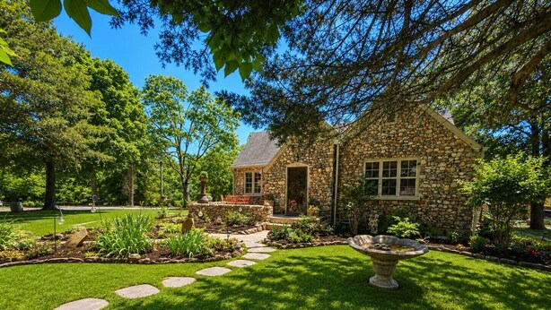 A stone house with a stone pathway leading to the entrance, surrounded by a well-maintained lawn and garden. - Rock Cottage Gardens B&B (Eureka Springs)