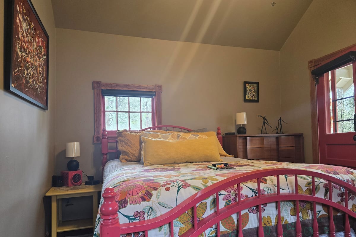Een slaapkamer met een bed, nachtkastje, dressoir, raam en deur.