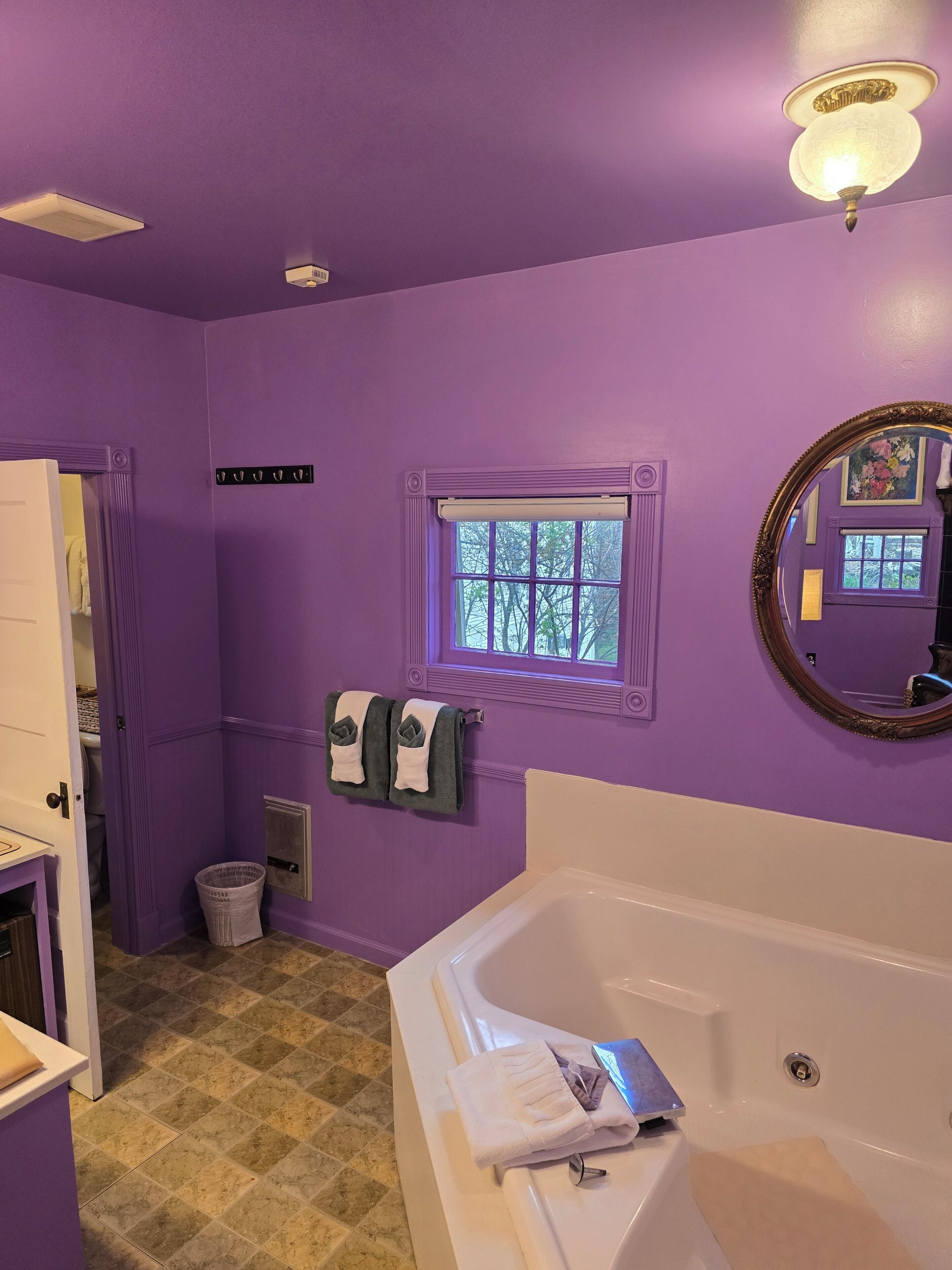 Une salle de bain avec des murs violets, une fenêtre, une baignoire, un miroir et un porte-serviettes.