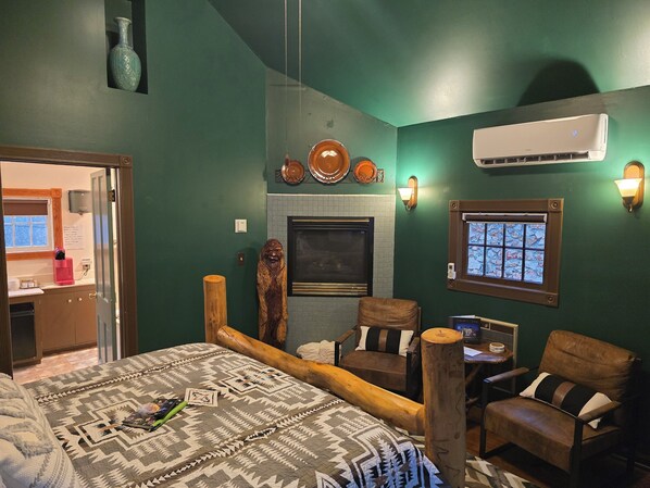 A room with a bed, a wooden headboard, a fireplace, a wall-mounted air conditioner, and a window with a view.