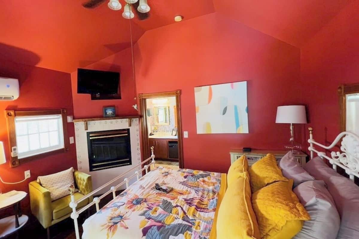 Een kamer met een bed, een bank, een eettafel, een lamp, een spiegel en een open haard.