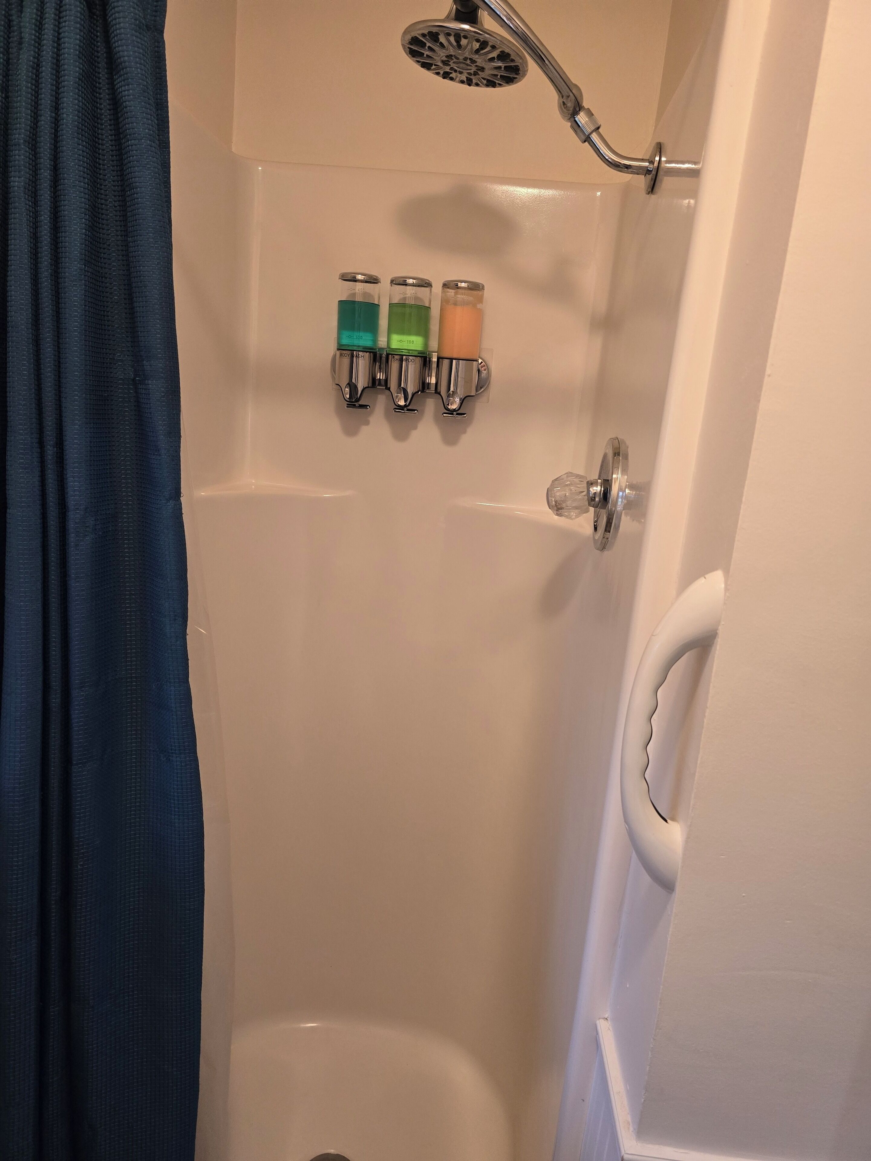 A shower with a handheld showerhead, three soap dispensers, and a white bathtub.