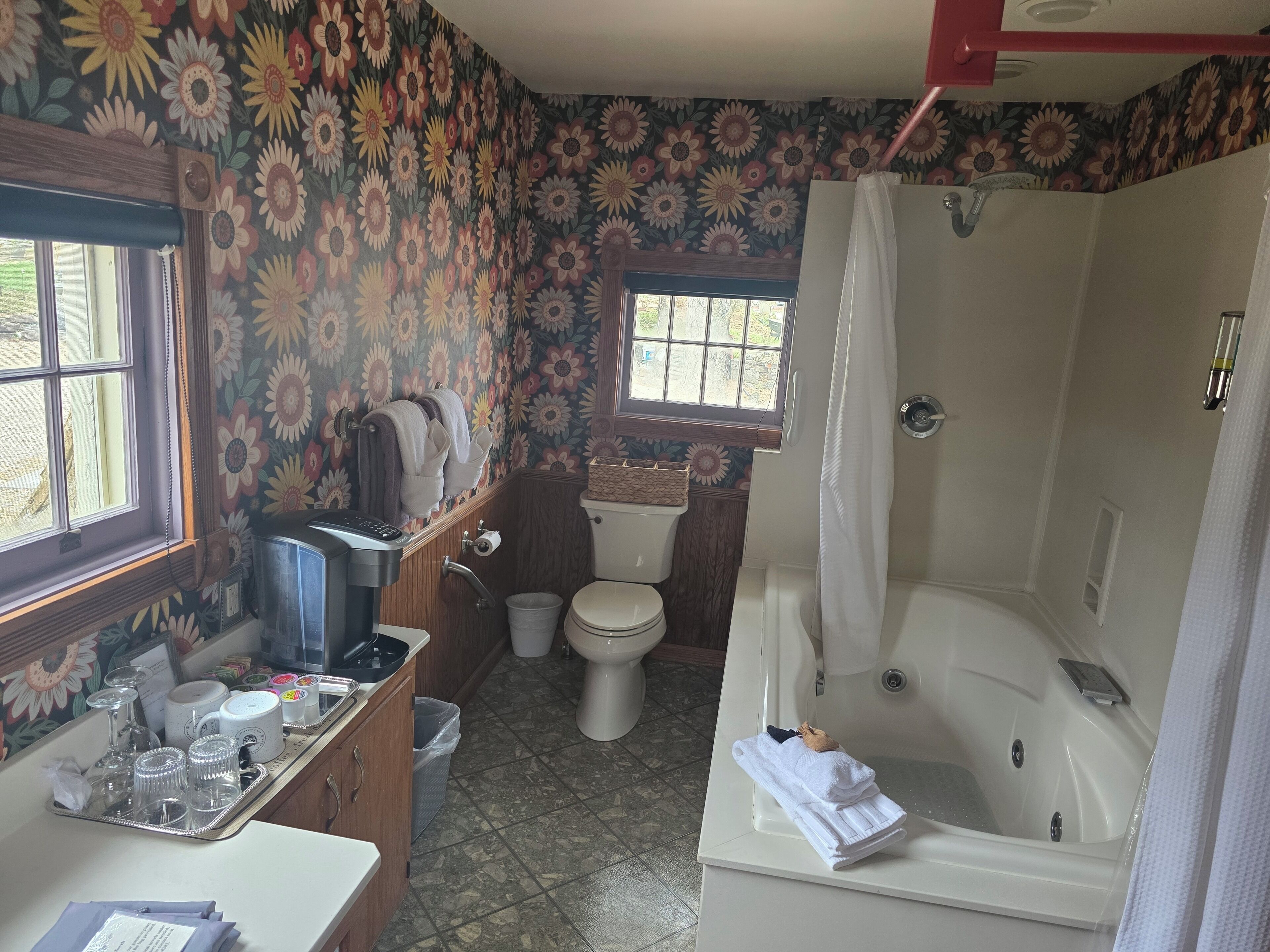 A bathroom with a floral wallpaper, a toilet, a bathtub, and a window.