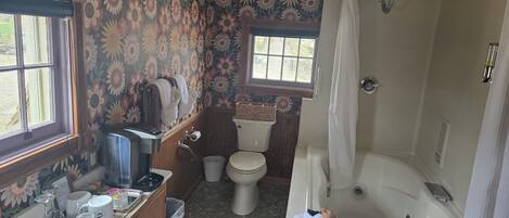A bathroom with a floral wallpaper, a toilet, a bathtub, and a window.