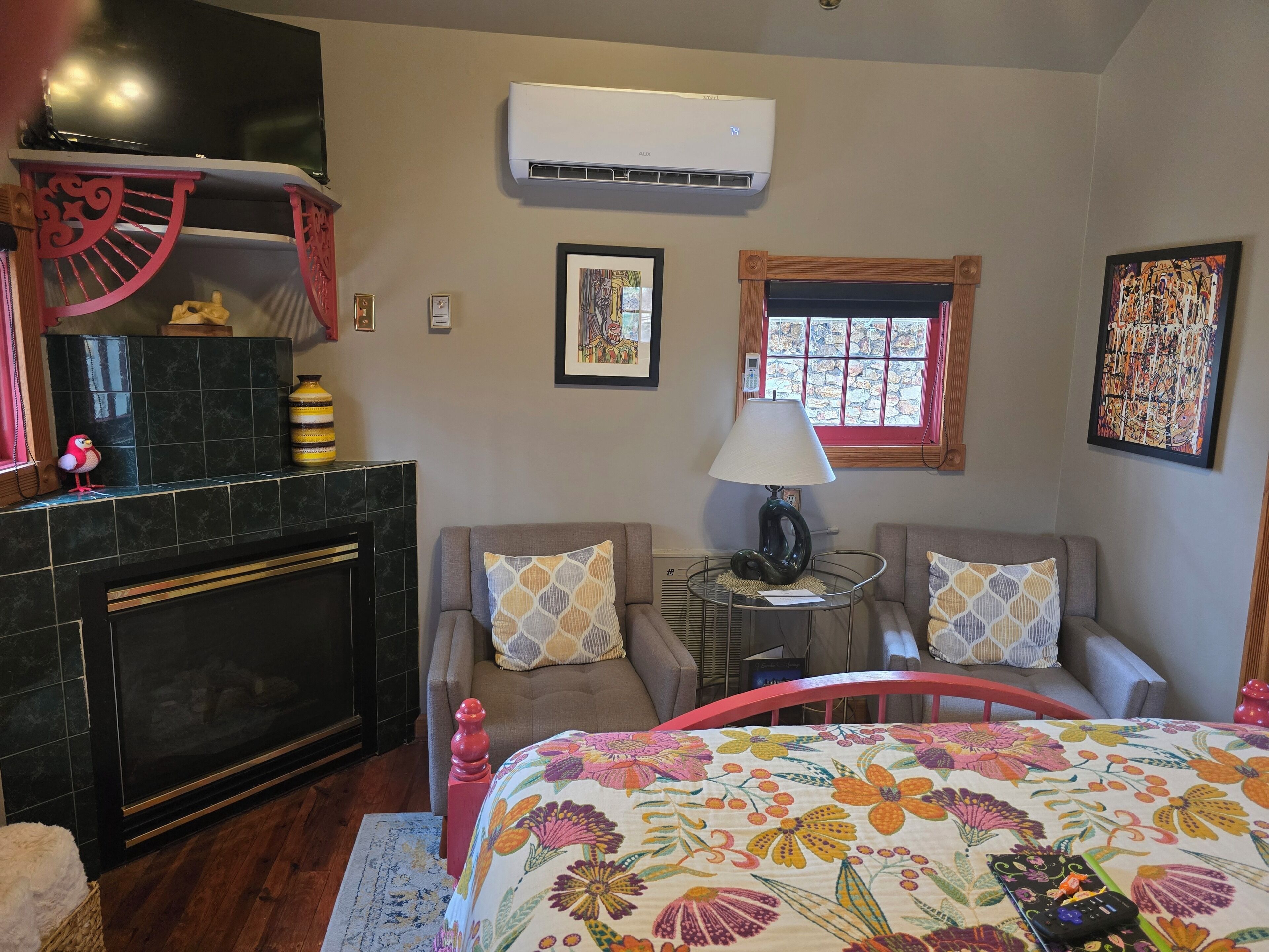 A bedroom with a fireplace, a bed with floral bedding, a small table with a lamp, and a window with a view.