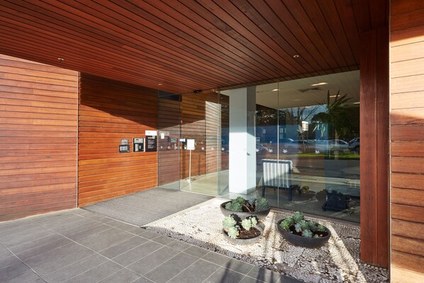 A modern building entrance with wooden paneling, glass doors, and potted plants.