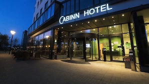 Exterior del hotel Cabinn, con entrada de vidrio, zona de estar al aire libre y fachada bien iluminada.