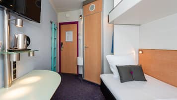 A modern hotel room with a bed, a small table with a kettle, a TV mounted on the wall, and a door with a purple frame.