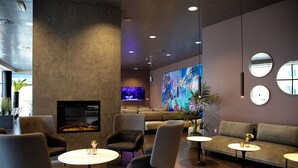 Un área de estar moderna con sofás, sillas y mesas, un televisor de pantalla plana y un cuadro abstracto grande en la pared.
