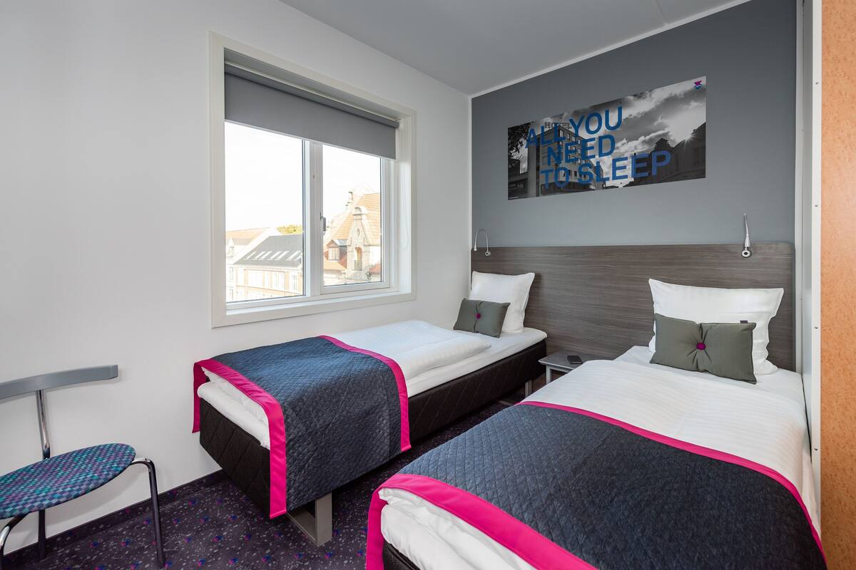 A hotel room with two beds, a window, and a wall-mounted artwork.