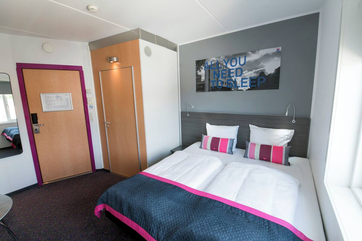 A hotel room with a bed, a desk, a wardrobe, and a bathroom door.
