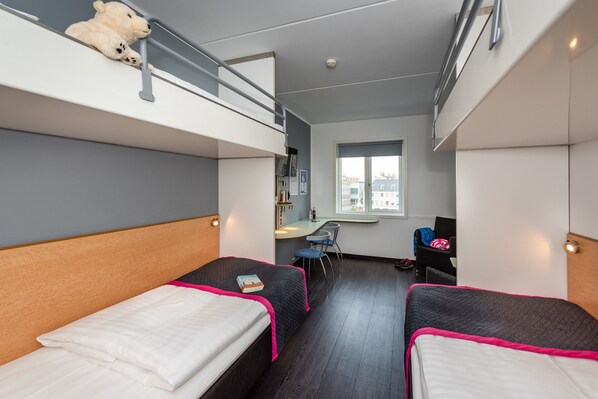 A compact hotel room with bunk beds, a desk, and a window.