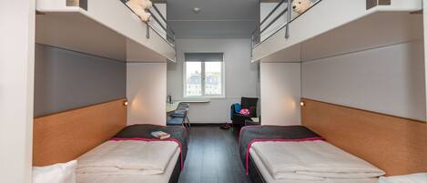 A dormitory room with two single beds, a desk, a chair, and a window.