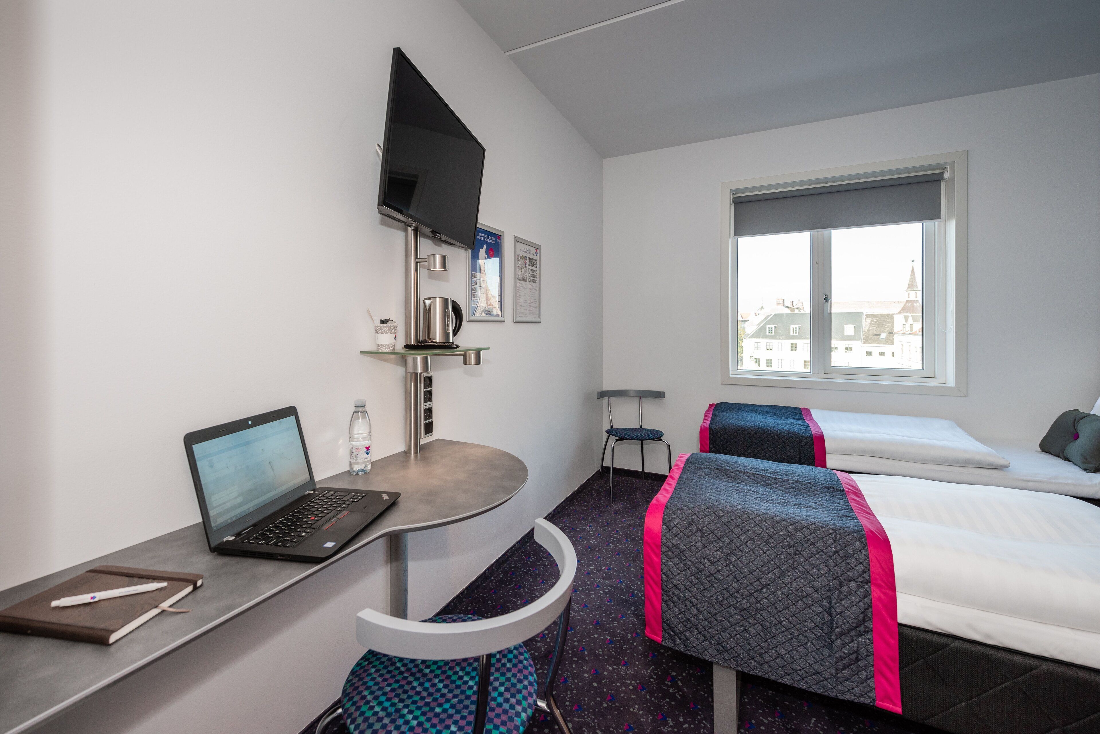Habitación de hotel con escritorio, ordenador portátil, cama y ventana con vistas a la ciudad.